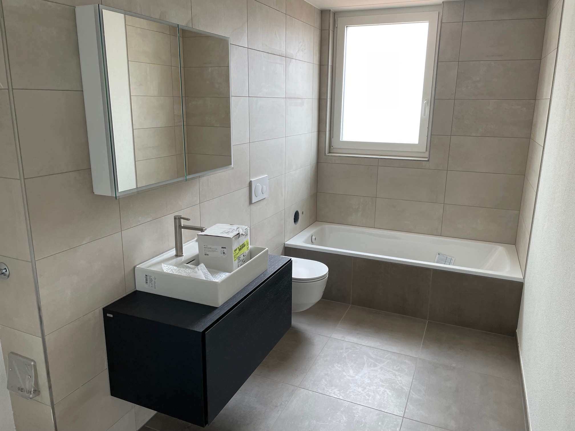 Bad mit beigen Platten, Badewanne und schwarzem Waschtisch